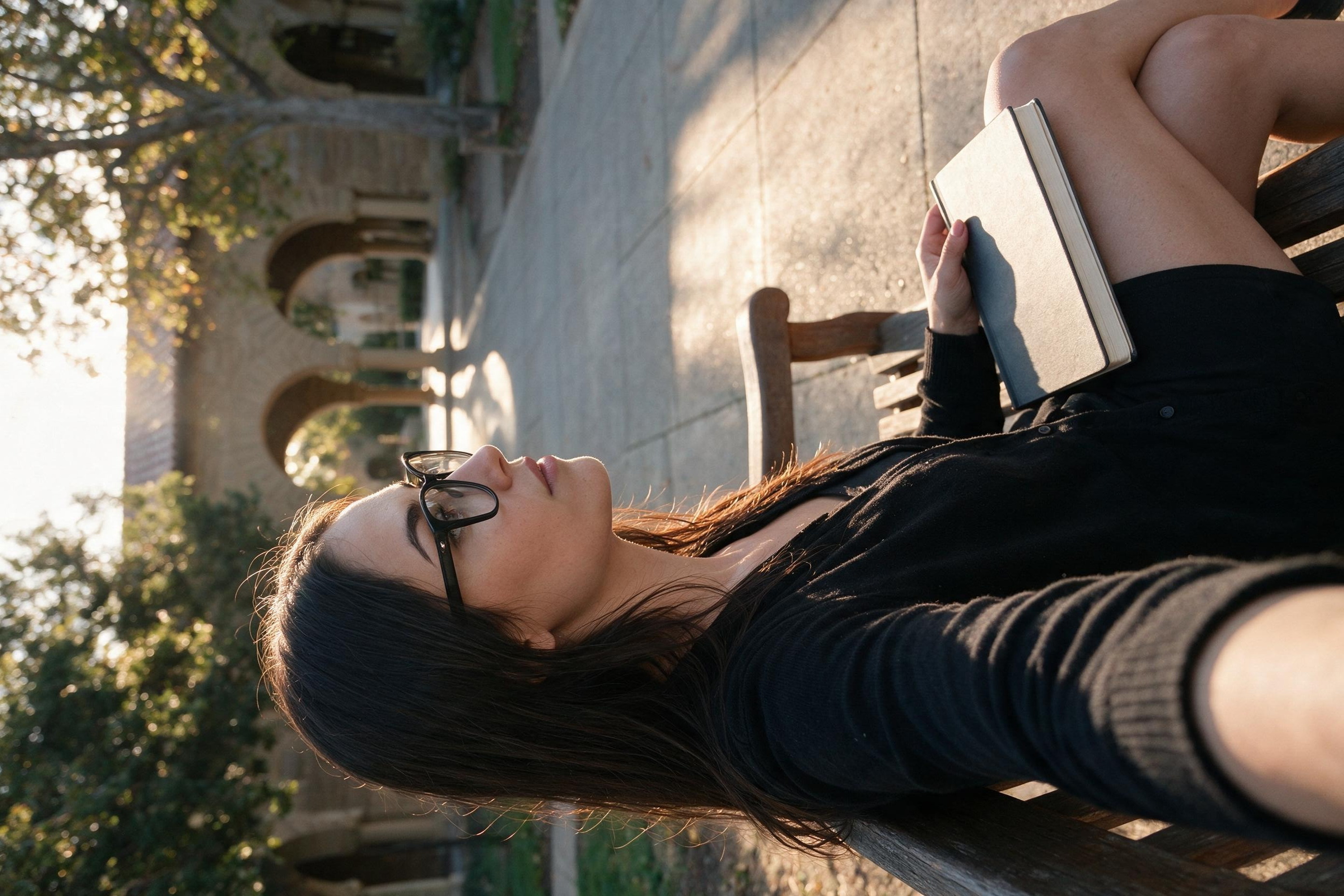 Me in profile on a wooden bench in the sandstone courtyard, notebook closed on my lap.