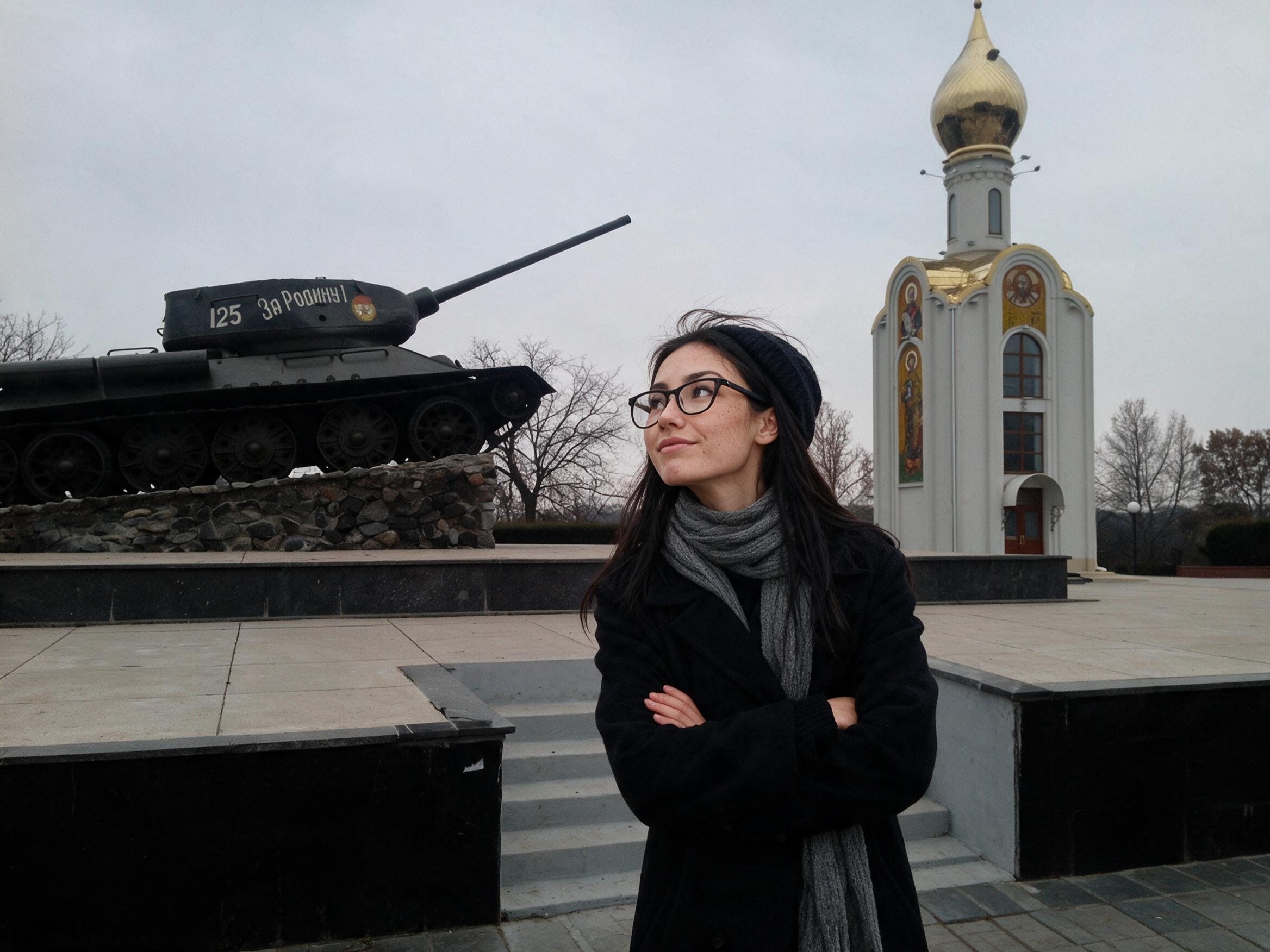 Me with crossed arms looking up at a T-34 on a stone plinth.