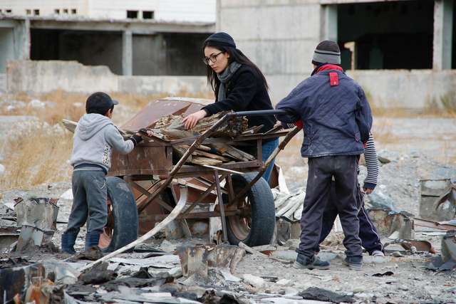 Me helping push a rusty cart of firewood; two kids pulling ahead through ruins.