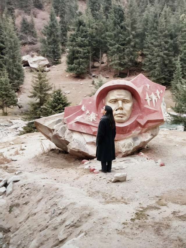 Me in a long black coat before the boulder with the golden cosmonaut relief, autumn valley.