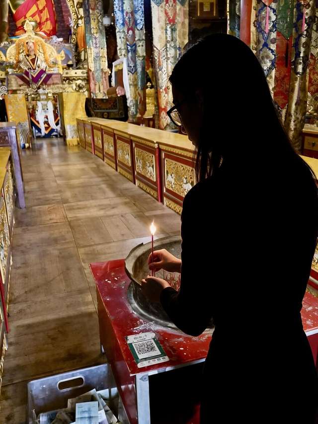 Me silhouetted, planting a glowing incense stick against the monastery's golden shrine light.