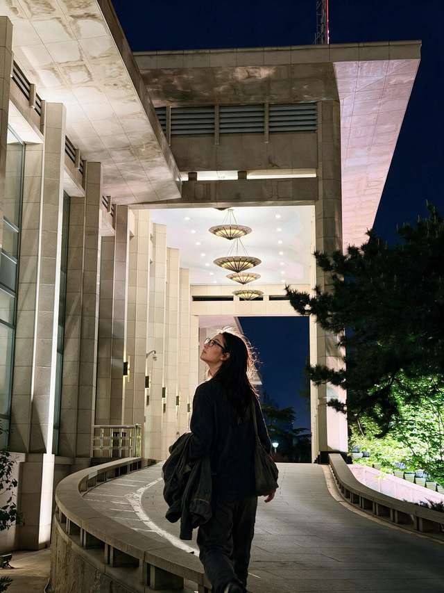 Me walking under the umbrella-shaped lamps on the hotel's curved night drive, floodlit pines beside.