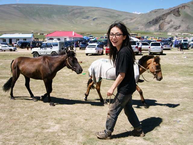 Me leading a racehorse with a white blanket at a naadam, glancing back.