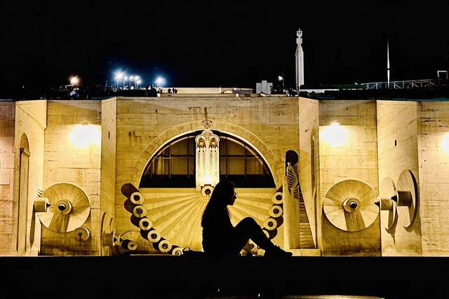 My silhouette at the Yerevan Cascade at night, carved wall floodlit behind.