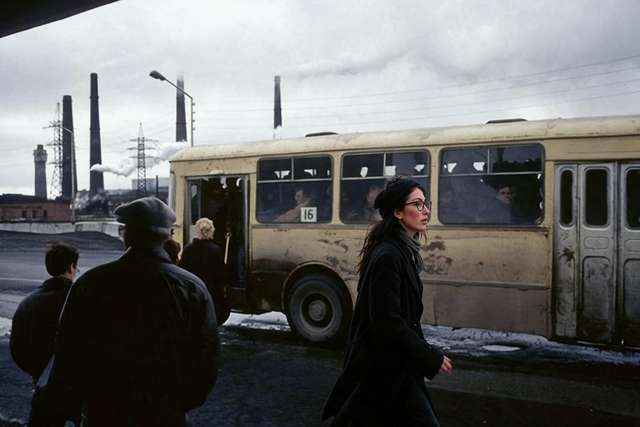 Me walking past a battered old trolleybus, factory smokestacks behind.