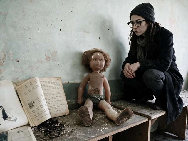 Me crouching near an old doll and open primer on a bench in the abandoned kindergarten.