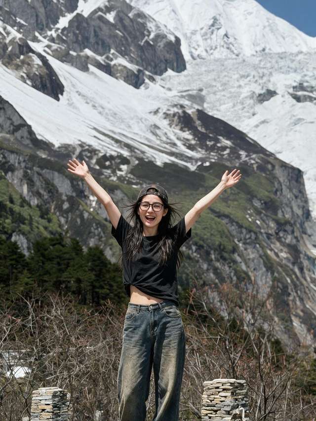 Me on a boulder, both arms up, before an enormous snow-covered glacier flank.