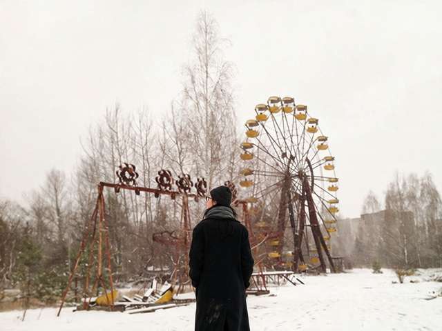 Me standing small under the rusted yellow ferris wheel of Pripyat in the snow.